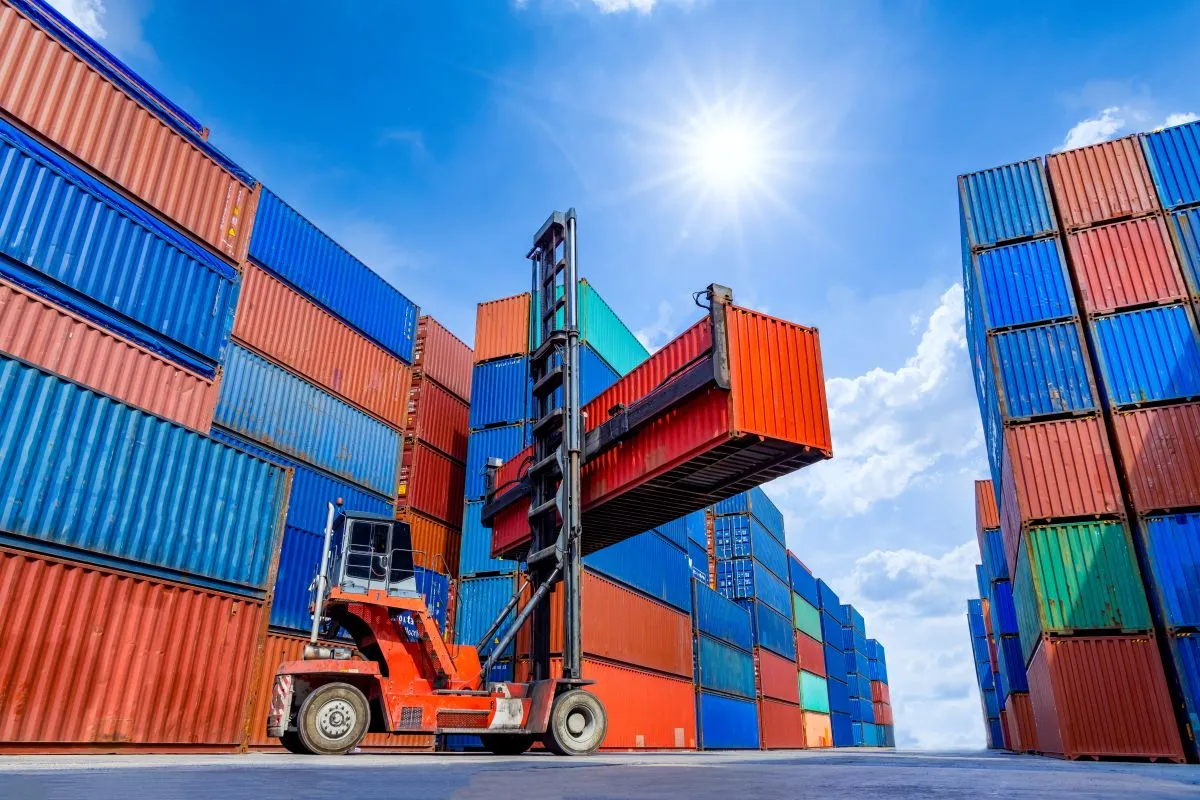 Solid Cargo GmbH - Internationalen Handel - Containerstaplerkran hebt gestapelte Container auf dem Betriebsgelände an; Containerverladung von Frachtgut in einem Import- und Exportlogistikunternehmen; Industrielogistik und Transport